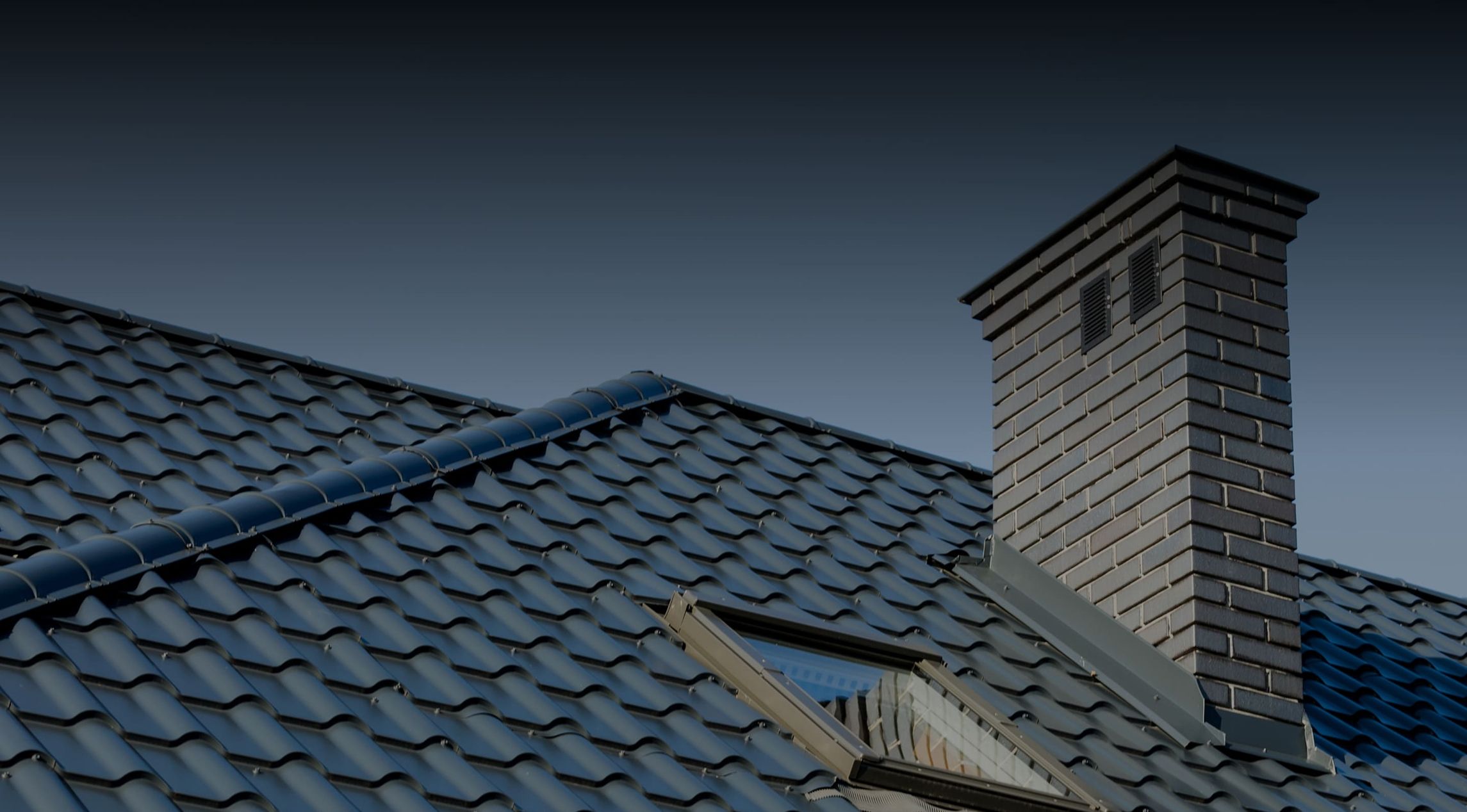 Schiefergedecktes Hausdach mit gemauertem Schornstein unter blauem Himmel